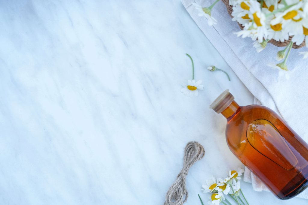 Kamillenblüten und Flasche mit ätherischem Öl als Symbol für pflanzliche Hausmittel.