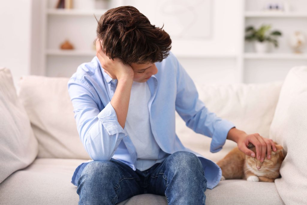 Trauernde Person sitzt neben einer Katze auf dem Sofa und bedeckt ihr Gesicht